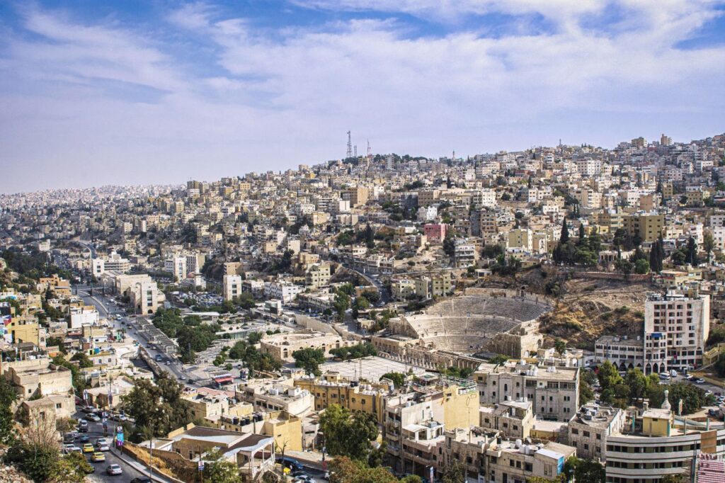 Explore Amman's urban landscape and ancient Roman amphitheater in a stunning aerial view.