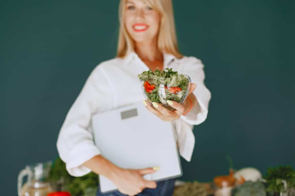 A woman with a vibrant smile offering a fresh salad bowl, promoting healthy eating.