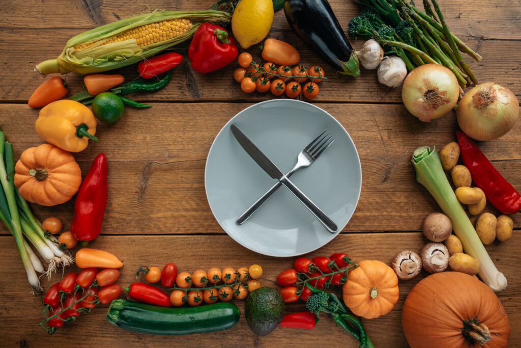 Top view of fresh vegetables creatively arranged around an empty plate on a wooden table.