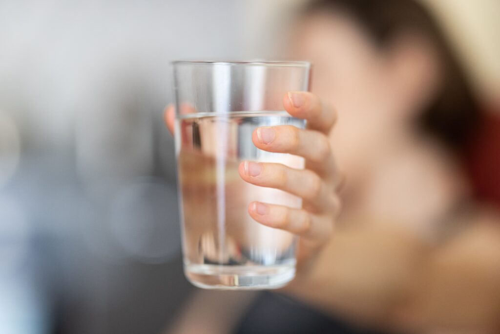 A hand holding a clear glass of water with a blurred background for health and hydration concept.